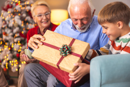 Happy multi-generation family spending Christmas day together at home, grandparents giving Christmas present to their grandsonの写真素材