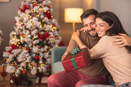 Happy couple in love celebrating Christmas day at home, hugging while exchanging presentsの写真素材