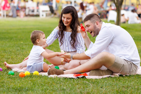 Beautiful young parents having picnic in the park with their cute little baby boy, sitting on the blanket and playing with colorful ballsの写真素材