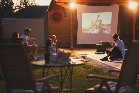 Group of cheerful young friends having fun eating popcorn, drinking cocktails and watching a movie...
