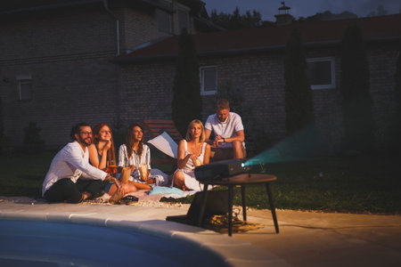 Group of cheerful young friends having fun eating popcorn, drinking cocktails and watching a movie...