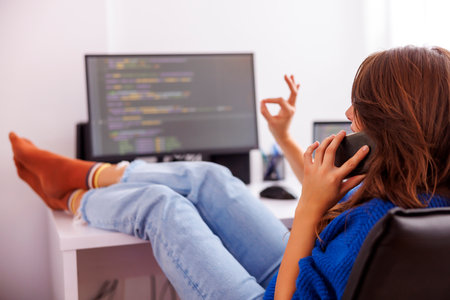 Female web developer having phone conversation while working in home office; female programmer speaking on the phone while working remotely from homeの写真素材