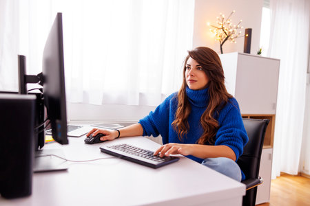 Female freelancer working in home office sitting at her desk, using desktop and laptop computers; female web developer working remotely from homeの写真素材