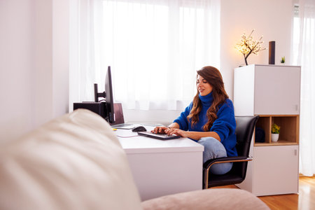 Female freelancer working in home office sitting at her desk, using desktop and laptop computers; female web developer working remotely from homeの写真素材