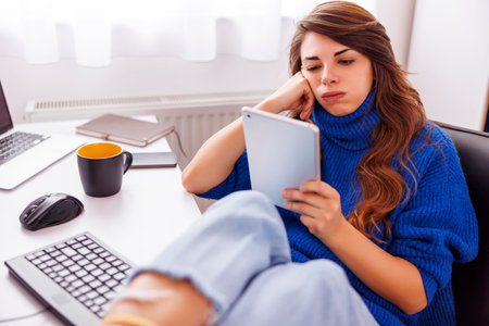Anxious female freelancer using tablet computer while working in home office; female software developer doing code review anxious because of critical malfunctionの写真素材