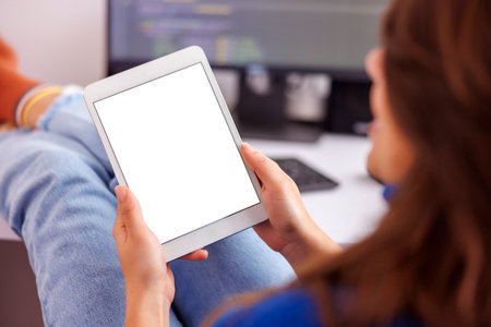 Female web developer holding empty screen tablet computer while working in home office; female programmer using tablet computer while working remotely from homeの写真素材