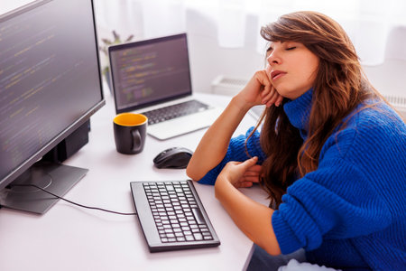 Female programmer sleeping at her desk in home office while working remotely from home, tired while working overtime to meet the project deadlineの写真素材