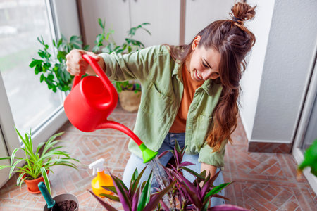 Beautiful young woman enjoying leisure time at home, relaxing while watering houseplantsの写真素材