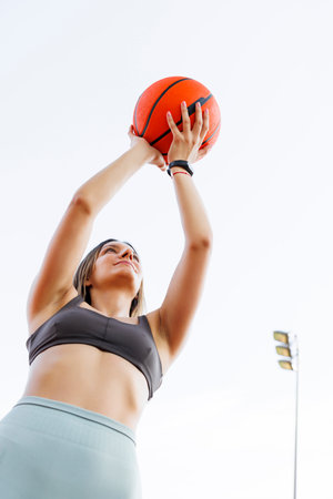 Low angle view of young woman in sportswear playing basketball as morning workout routineの写真素材
