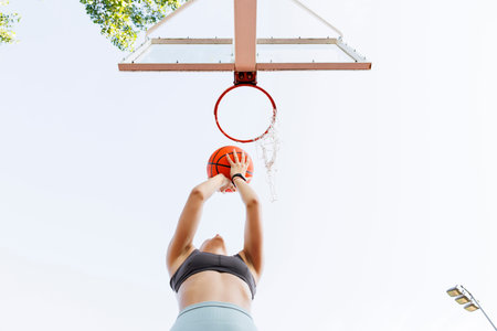 Low angle view of young woman in sportswear shooting hoops playing basketball as morning workout...