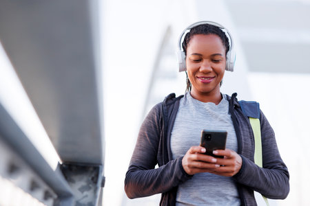 Active woman in sportswear wearing headset listening to the music and using smart phone, carrying gym bag while going for morning jogging or outdoor workout sessionの写真素材