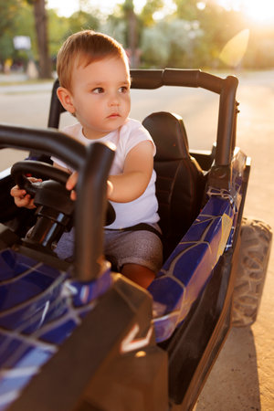 Cute little toddler boy having fun driving battery powered toy car while spending summer afternoon with parents outdoorsの写真素材