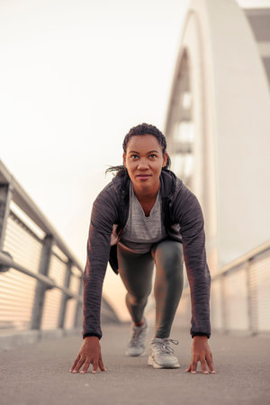 Active woman in sportswear warming up and stretching out, taking low start pose before morning jogging or outdoor workout sessionの写真素材