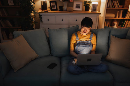 High angle view of woman sitting on living room couch working remotely from home late at night using laptop computerの写真素材
