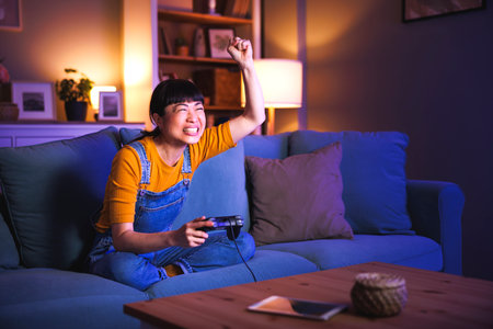 Beautiful woman having fun at home late at night playing video games, celebrating after winning the gameの写真素材