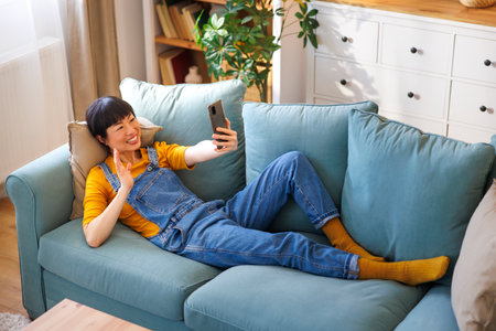 High angle view of woman having video call using smart phone while relaxing at homeの写真素材