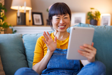 Beautiful woman having video call using tablet computer while relaxing at homeの写真素材