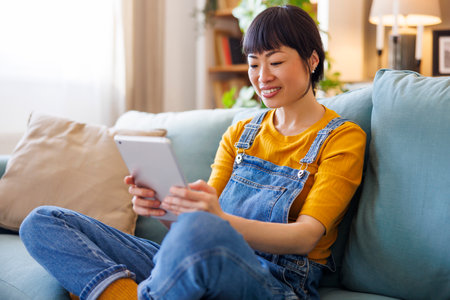 Beautiful woman reading an ebook using tablet computer while relaxing at homeの写真素材