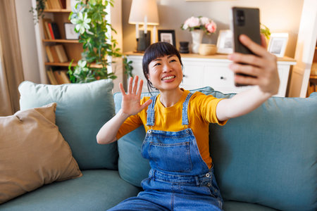 Beautiful Asian woman having video call using smart phone while enjoying leisure time and relaxing...