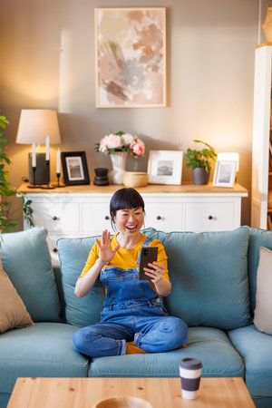 Beautiful Asian woman having video call using smart phone while enjoying leisure time and relaxing at homeの写真素材