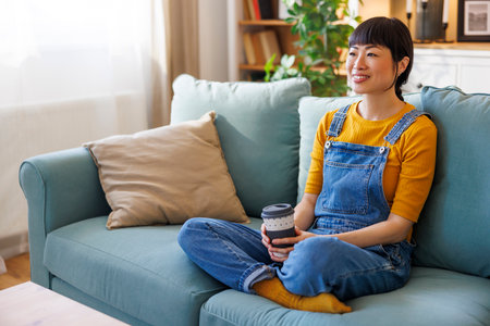 Beautiful Asian woman relaxing and drinking coffee while enjoying leisure time at homeの写真素材