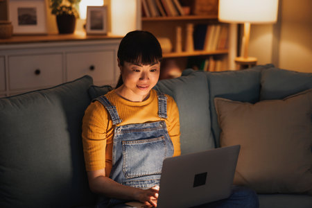 Female freelancer sitting on living room couch working from home using laptop computer late at nightの写真素材