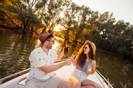 Beauitful young couple in love enjoying summer vacation, pouring glasses of champagne celebrating anniversary while sailing to the sunset on a boatの写真素材