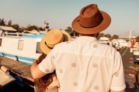Back view of young couple in love hugging while taking a walk by the river on the city marina docks, enjoying hot summer day outdoorsの写真素材