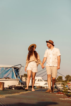 Low angle view of beautiful young couple in love holding hands while walking down river docks in city marina, enjoying hot summer day outdoorsの写真素材