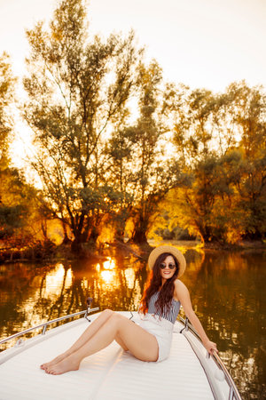 Beautiful young woman relaxing while on summer vacation sailing to the sunset on a boatの写真素材