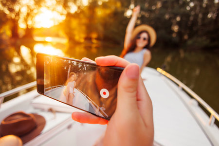 Detail of man photographing woman using smart phone while sailing to sunset on a boat, relaxing and...
