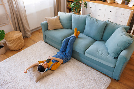 High angle view of cheerful mature Asian woman lying on the living room floor having fun listening to the music, singing and dancing while enjoying leisure time at homeの写真素材