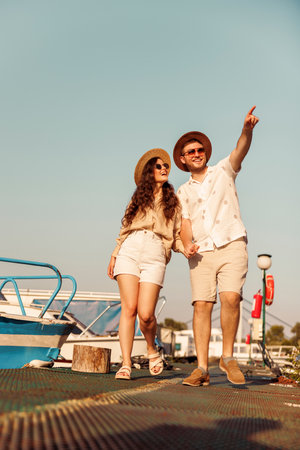Low angle view of young couple in love holding hands while taking a walk by the river on the city marina docks, enjoying hot summer day outdoorsの写真素材