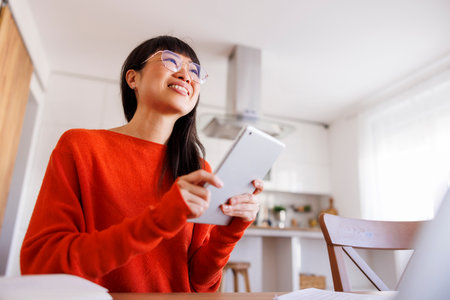 Mature Asian woman using tablet computer while working remotely from homeの写真素材