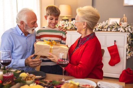 Family gathered around table having Christmas dinner at home, grandparents giving Christmas present...