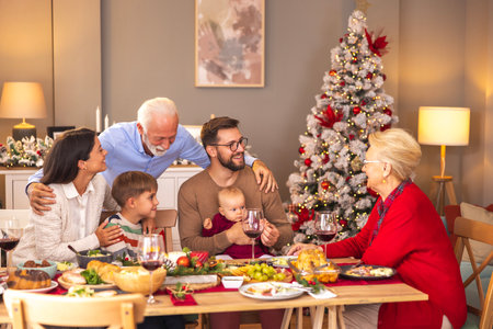 Happy multi-generation family gathered around the table, having Christmas dinner all together at home, speaking to each other and laughingの写真素材