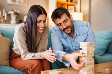 Beautiful young couple in love having fun playing block stacking balance game pulling and pushing wooden blocks from the sturdy tower in order not to crush itの写真素材