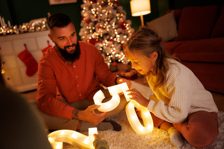 Young parents and children having fun celebrating New Year at home, holding illuminative numbers...