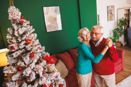 Happy senior couple having fun celebrating New Year at home, dancing by nicely decorated Christmas treeの写真素材