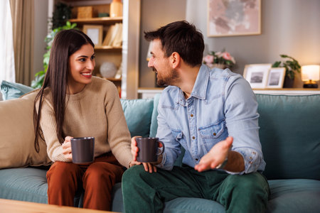 Beautiful happy couple in love having fun drinking coffee and relaxing at home, enjoying their leisure time togetherの写真素材