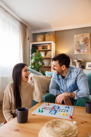 Beautiful young multi-ethnic couple in love having fun playing ludo board game while relaxing and enjoying leisure time together at homeの写真素材