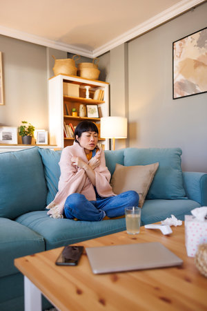 Sick woman having flu and fever covered with blanket relaxing at home while on sick leaveの写真素材