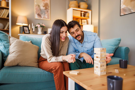 Beautiful young couple in love having fun playing block stacking balance game while relaxing and enjoying spending leisure time together at homeの写真素材