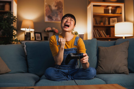 Beautiful woman having fun at home late at night playing video games, celebrating after winning the...