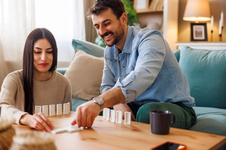 Beautiful young multi-ethnic couple in love having fun playing dominoes enjoying leisure time together at home and relaxingの写真素材
