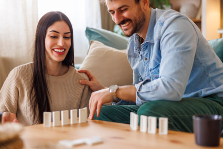 Beautiful young multi-ethnic couple in love having fun playing dominoes enjoying leisure time together at home and relaxingの写真素材
