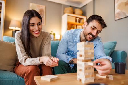 Beautiful young couple in love having fun playing block stacking balance game pulling and pushing wooden blocks from the sturdy tower in order not to crush itの写真素材
