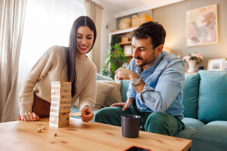 Beautiful young couple in love having fun playing block stacking balance game while relaxing and enjoying spending leisure time together at homeの写真素材