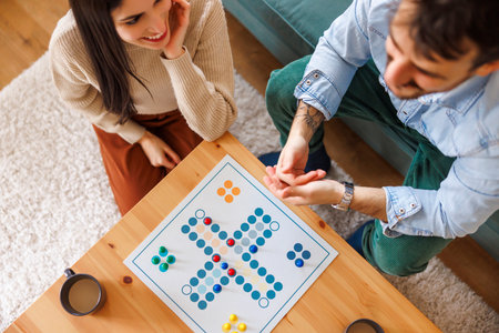 High angle view of beautiful young multi-ethnic couple in love having fun playing ludo board game...