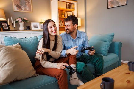 Beautiful young couple in love having fun playing video games while relaxing and enjoying spending leisure time together at homeの写真素材